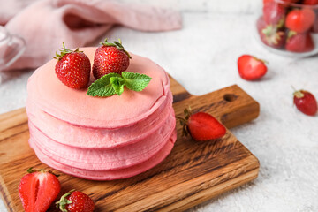 Wall Mural - Wooden board with tasty pink pancakes and strawberry on light background, closeup