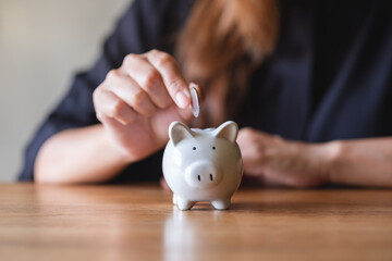 Closeup image of a woman putting coin into piggy bank for saving money concept