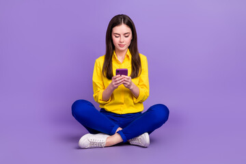 Sticker - Portrait of beautiful trendy focused girl sitting using device smm post isolated over bright violet purple color background