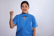 Portrait of a cheerful female nurse raising her fist against white background