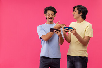 Portrait of two teenage boys playing games on Smartphone while standing against pink background