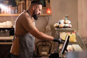 Profile view male barista at counter using cashbox computer in cafe store. Indian Waiter in apron working in coffee shop.small business, people and service