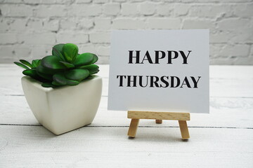 Wall Mural - happy thursday text on wooden easel standing on white brick wall and wooden background