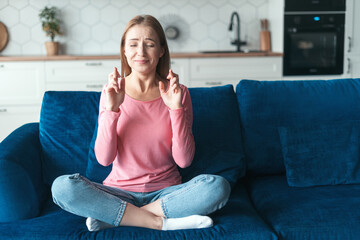 Woman with crossed fingers gesture, closes eyes at home