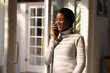 © Wavebreak Media - Happy young african american woman speaking on smart phone while standing by window at home