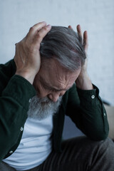 Wall Mural - stressed senior man with beard touching head while suffering from headache at home.