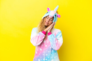 Wall Mural - Girl with curly hair wearing a unicorn pajama isolated on yellow background making sleep gesture in dorable expression