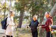 © Татьяна Волкова - Smiling woman sports trainer with group of people talking, explaining posture for Nordic walking with sticks in forest
