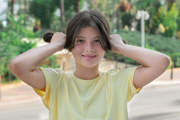 A young girl holds hair in her hands in a ponytail.