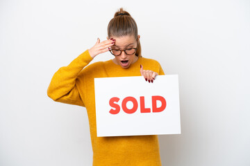 Wall Mural - Young caucasian woman isolated on white background holding a placard with text SOLD with surprised expression