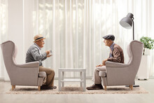 Elderly Men Sitting In Armchairs And Having A Conversation In A Living Room