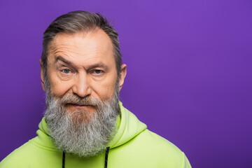 Wall Mural - skeptical senior man moving eyebrow while looking at camera on purple background.
