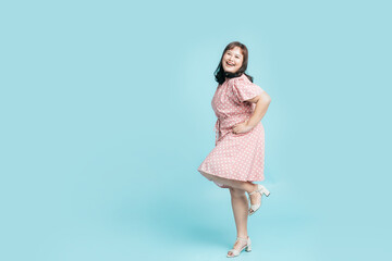 Full length Confidence cheerful beautiful smile Asian woman plus size in pink pastel dress on isolate light blue studio background. Fashion young female chubby confident concept.