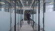© Synthex - Back view of office worker walking along hall with glass doors, corporate business