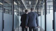 © Synthex - Two businessmen walking along office building corridor, business meeting with partners