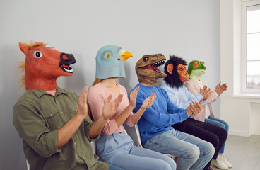 Diverse young people employees in funny animals rubber head masks sit in line clap hands show appreciation. Smiling unknown workers in queue applaud. Employment concept.