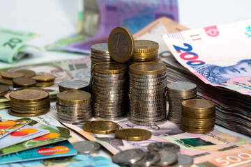 Stack of credit cards with Ukrainian hryvnia cash and euro coins, close-up view.