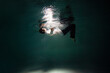 Sink. A young guy in a white shirt falls into the water, a photo from under the water. The concept of falling down, diving to the depth, contrasting dark photo