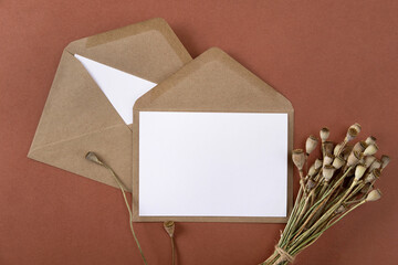 Wall Mural - Blank greeting cards and envelopes with dry flowers on brown background. Blank paper sheet cards with mockup copy space. Minimal workplace composition. Flat lay, top view