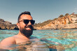 Happy man in sunglasses, bathing in the blue sea and smiling