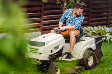 Wall Mural - Professional gardener driving a riding lawn mower in a garden. Industrial landscaping works.