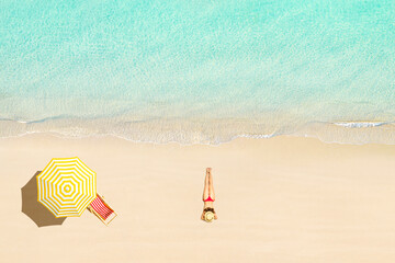 Top view of woman in bikini and straw hat lying and sunbathes near wooden sunbed, lounge and yellow umbrella on tropical Seychelles sea sand beach. Aerial, drone view