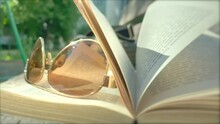 Sunglasses Book Slo MoSoft Focus Of The Sunglasses On An Open Book. The Pages Of Books Are Moving In The Light Breeze On A Sunny Day. Vacation In The City. Rest And Pleasure. Urban Summer Background. 