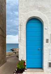  Closed and arched blue colored entrance door with stripes and white wall and succulents near the coastline
