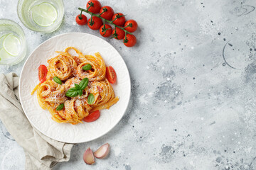 Tasty appetizing classic italian tagliatelle pasta with tomato sauce, cheese parmesan and basil on plate on light table. View from above, horizontal. Top view with copy space