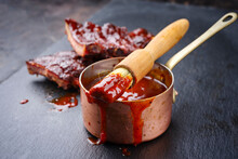 Hot And Spicy Barbecue Sauce In A Casserole As Close-up With Spare Ribs In Background