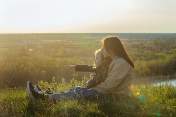 family on a walk at sunset outside the city, mom holds her daughter in her arms, they admire nature