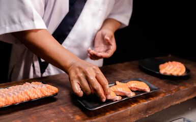 Chef's hand holding fresh piece of salmon.Closeup of chef hands preparing japanese food. Japanese chef making sushi at restaurant.Chef making traditional japanese sushi on wood board.