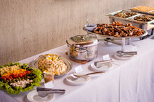 A Table With A Buffet Of Food Served In Stainless Steel Bowls With Salads And Meats
