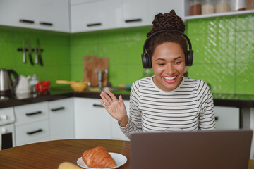 Wall Mural - happy mixed-race female wearing headphones waving hand while having video call online