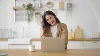 Wall Mural - Smiling asian young woman working on laptop at home office. Young asian student using computer remote studying, virtual training, e-learning, watching online education webinar at house