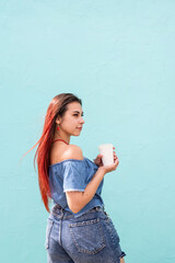 Wall Mural - cheerful trendy woman with red hair drinking coffee dancing on blue wall background at street