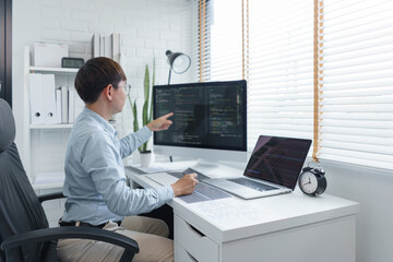 Wall Mural - software development concept, male programmer checking data codes on document and computer screen