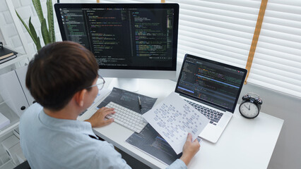 Wall Mural - software development concept, male programmer read data on document while programming on computer