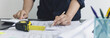 © Puwasit Inyavileart - Architectural building design and construction plans with blueprints, Young man was designing a building or architecture with a ruler, pen, pencil, tape measure, architect hat and other equipment.