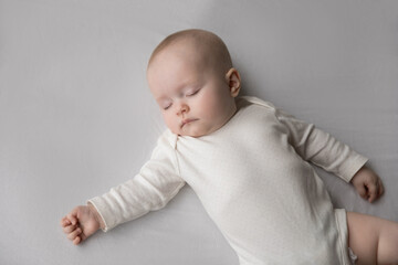 Close up above shot, calm three-month-old newborn baby in white bodysuit and dry diaper falling asleep, sleeping, lying on bed with eyes closed. Healthy day nap for children growth. Babyhood concept