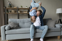 Loving Cheerful Father Play With Preschool 5s Laughing Son Lifts, Turned His Upside Down Feel Happy Spend Funny Weekend Leisure Together Sit On Sofa. Fatherhood, Playtime With Children At Home Concept
