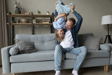 Loving cheerful father play with preschool 5s laughing son lifts, turned his upside down feel happy spend funny weekend leisure together sit on sofa. Fatherhood, playtime with children at home concept