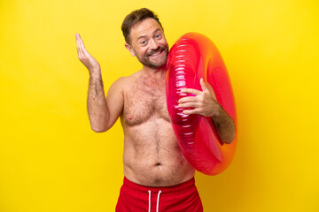 Wall Mural - Middle age caucasian man holding inflatable donut isolated on yellow background extending hands to the side for inviting to come