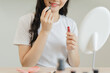 © Pormezz - Daily makeup routine, Asian young women looks in the mirror during applying lipstick on her lip.