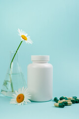 Wall Mural - A bottle of pills on a blue background. Flasks with medicinal plants. Place for text. Medical concept photo. Chamomile and pills