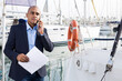 Man businessman communicates on a mobile phone with in the port near his yacht