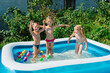 © Serhii - Three happy friends are splashing in an inflatable pool in the garden. Concept of summer season and recreation. Kids having fun together. Children playing and swimming in water on the backyard.
