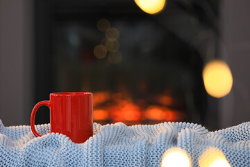 Poster - Cup of hot drink on knitted blanket near fireplace at home, space for text. Cozy atmosphere