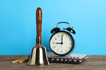 Wall Mural - Golden bell, alarm clock and school stationery on wooden table against turquoise background