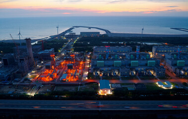 Aerial view of Tatan Power Plant in an industrial estate and wind turbines along the coast with jetties extruding into the sea under golden sunset sky, in Guanyin District, Taoyuan City, Taiwan